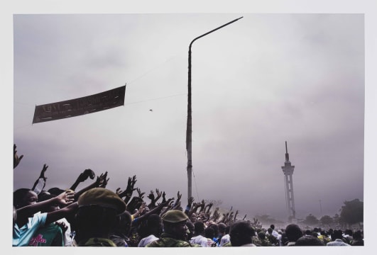 Guy Tillim; A Statue Of Patrice Lumumba Erected By Laurent Kabila, And An Unfinished Tower Built During The Mobutu Years, Look Down On Jean- Pierre Bemba Supporters As They Make Their Way To A Rally, Kinshasa, July 2006
