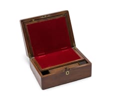 Wooden writing box with a brass inlay in the centre of the lid, brass hinges and small key, opening into two halves onto a red velvet rectangular surface. A latch opens the top half with a shallow storage space below for writing paper, envelopes and stamps. The bottom half consists of two parts, the bottom part a shallow drawer with a removable lid for storing pens, flanked by two cubicle spaces for storing ink bottles, the top part opens onto an