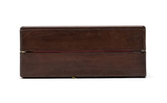 Wooden writing box with a brass inlay in the centre of the lid, brass hinges and small key, opening into two halves onto a red velvet rectangular surface. A latch opens the top half with a shallow storage space below for writing paper, envelopes and stamps. The bottom half consists of two parts, the bottom part a shallow drawer with a removable lid for storing pens, flanked by two cubicle spaces for storing ink bottles, the top part opens onto an